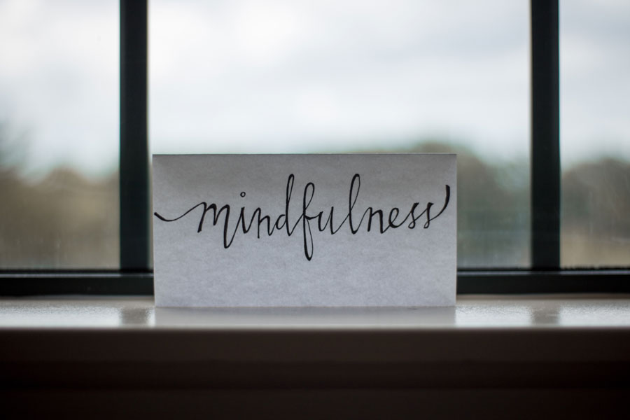 Ein Papierzettel lehnt an einem Fenster. Mit schwarzem Stift und verschnörkelter Schrift steht dort mindfulness.